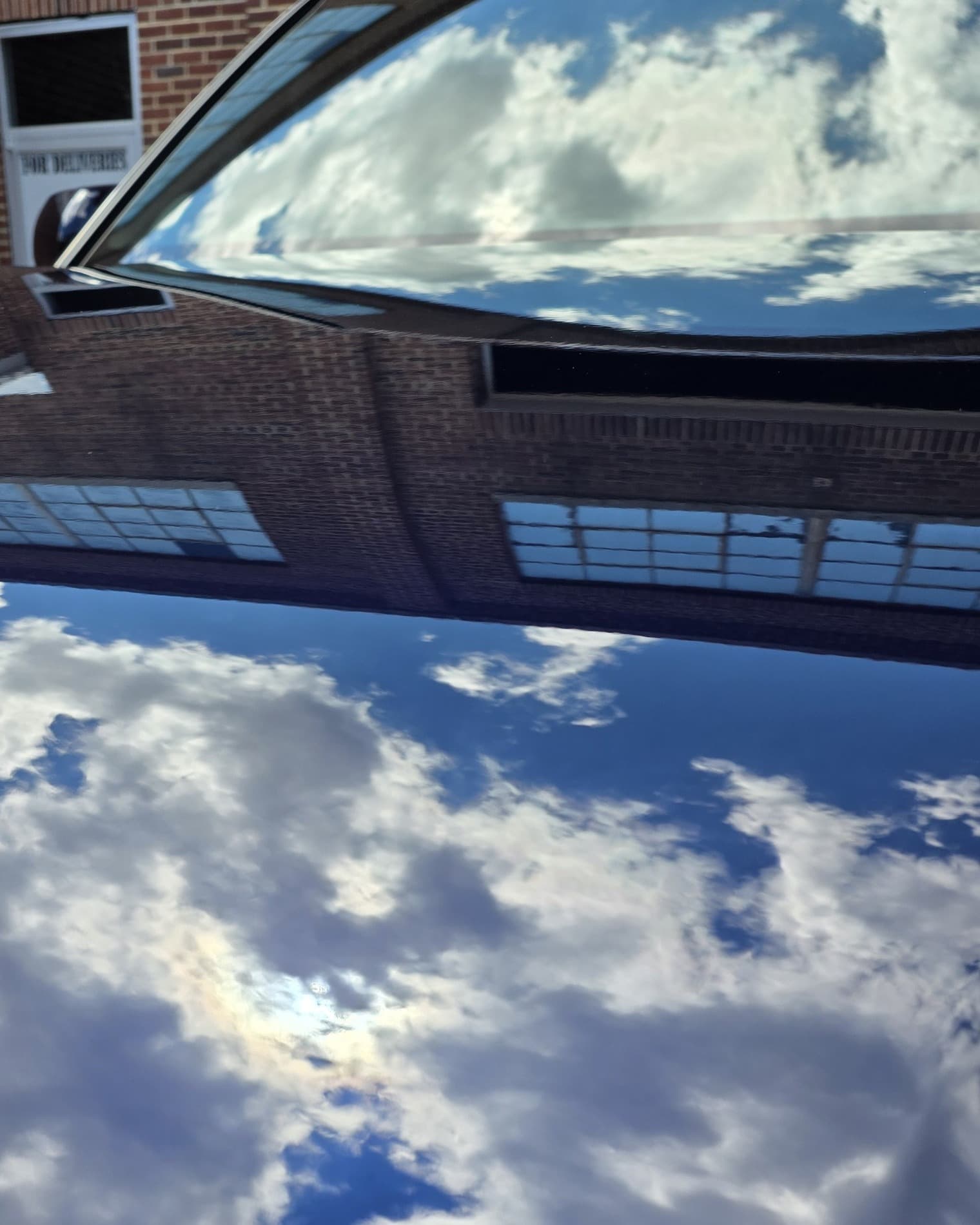 Sky and clouds mirrored in a flawless, corrected dark paint finish by Mr. G's Auto Care in Westminster, MD