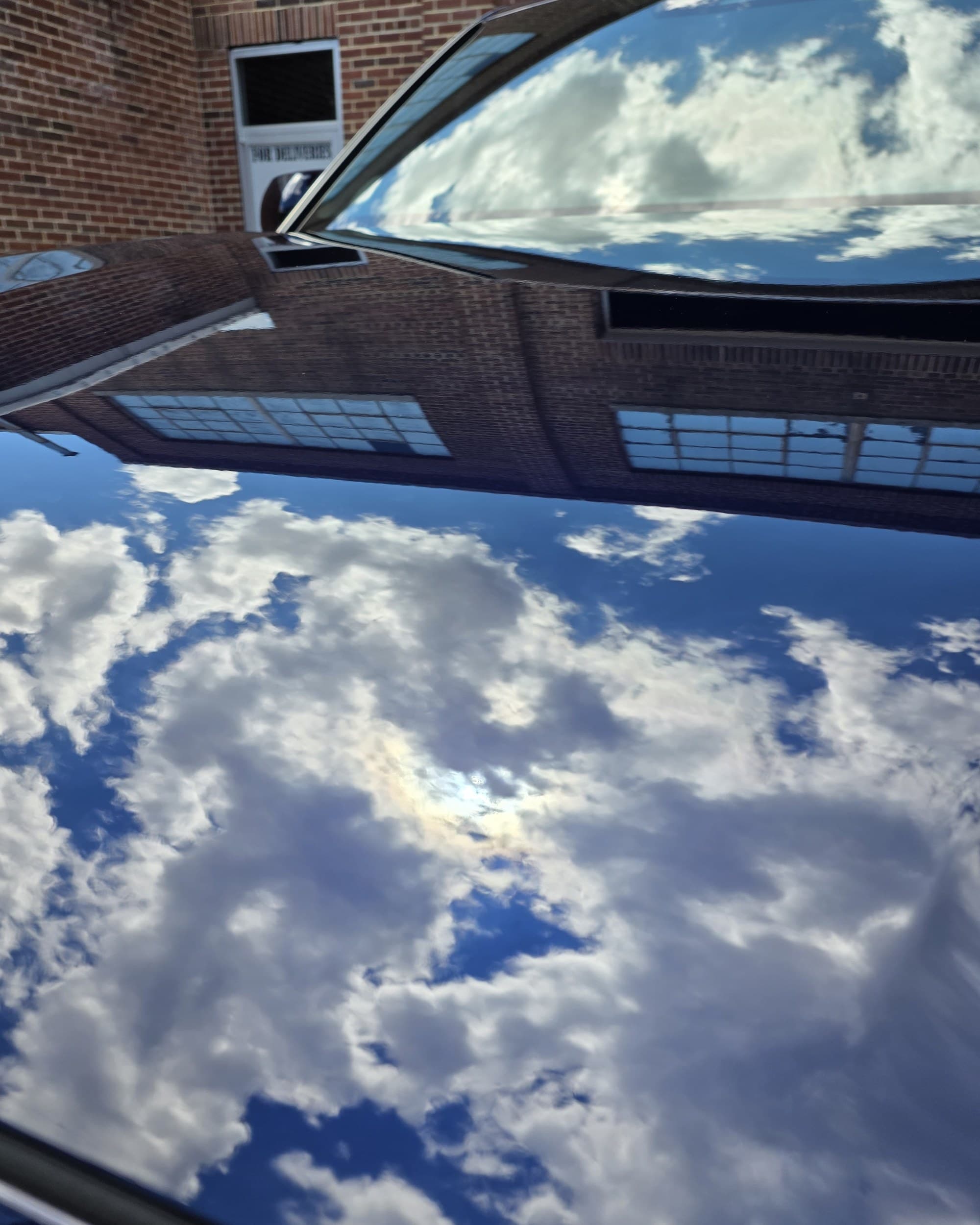 The hood of a navy Toyota Sequoia reflecting clouds and a brick building with mirror clarity after paint correction at Mr. G's Auto Care in Westminster, MD